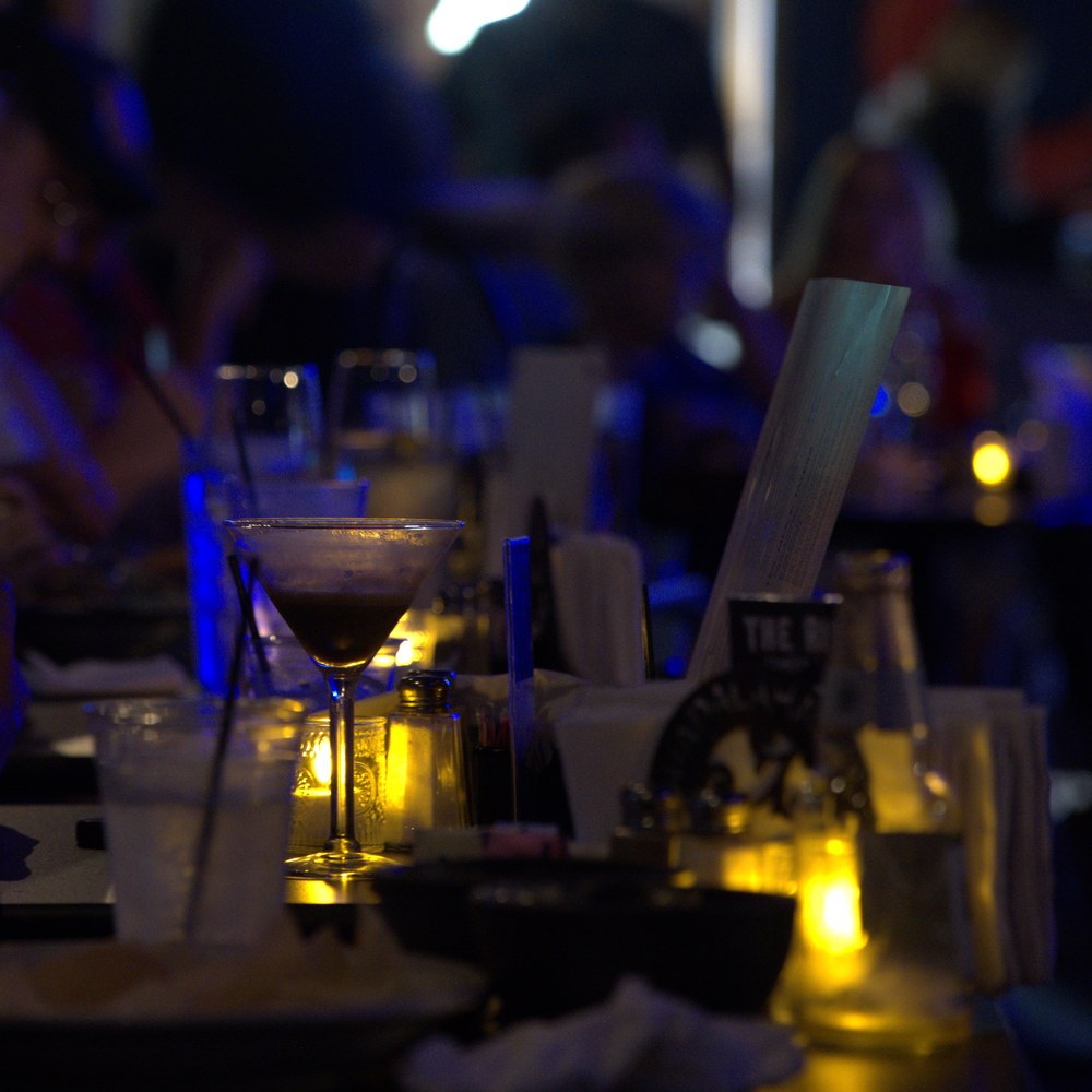 A cocktail on the bar with the room busy behind it